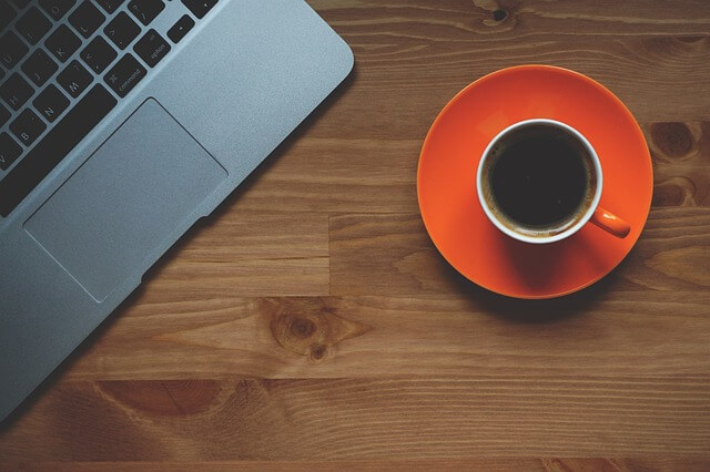 Coffee cup on orange saucer sitting on desk next to an open laptop