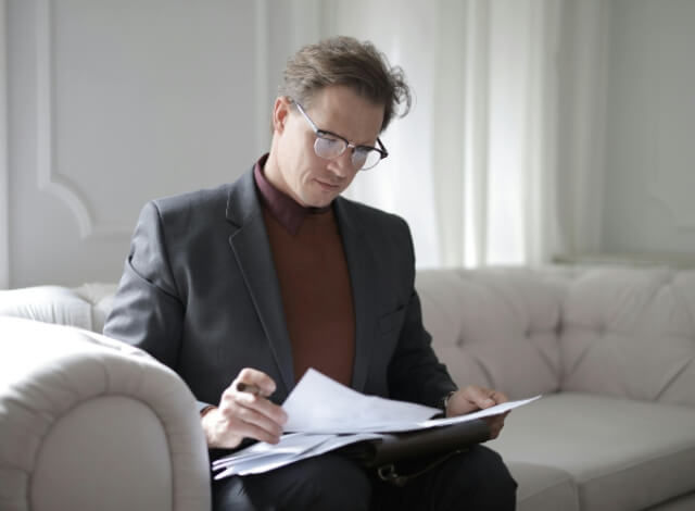 Man in business suit sitting on white couch reading through papers